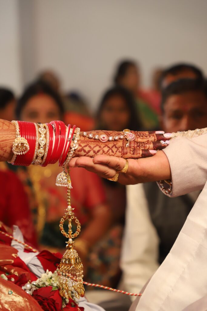 Close-up of bride and groom's hands during traditional Asian wedding ceremony with intricate henna designs.